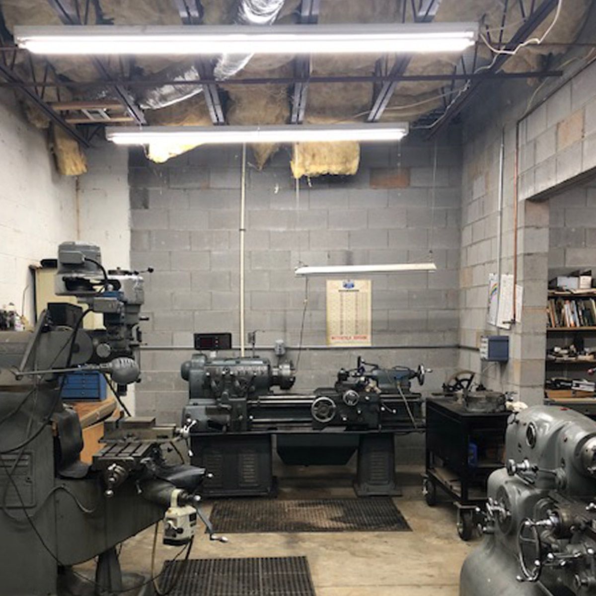 Industrial workshop with four-foot LED tubes in linear fluorescent fixtures providing bright task lighting over workbenches with tools and equipment showing improved color rendering and reduced shadows
