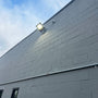 LUX LED Flood Light mounted on gray building wall shining bright under a clear sky at dusk