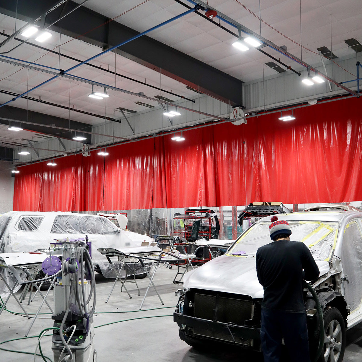 Industrial workspace illuminated by Linear LED High Bay – 2 CCT – 210/180/155W fixtures with covered vehicles and worker