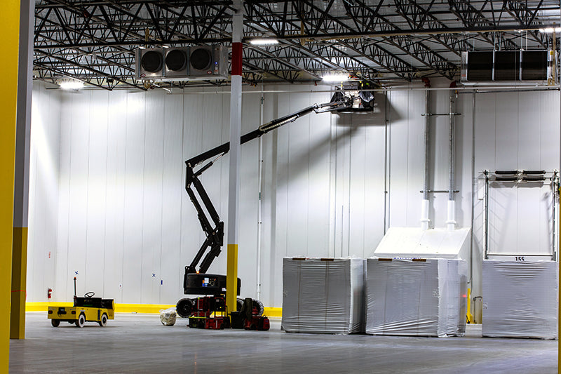 Scissor lift accessing high ceiling warehouse LED lighting fixtures demonstrating maintenance challenges at elevated mounting heights