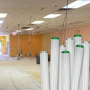 A bundle of fluorescent tubes that have been removed from fluorescent fixtures seen in the background; the fixtures have been retrofitted for LED lighting and are much brighter than before